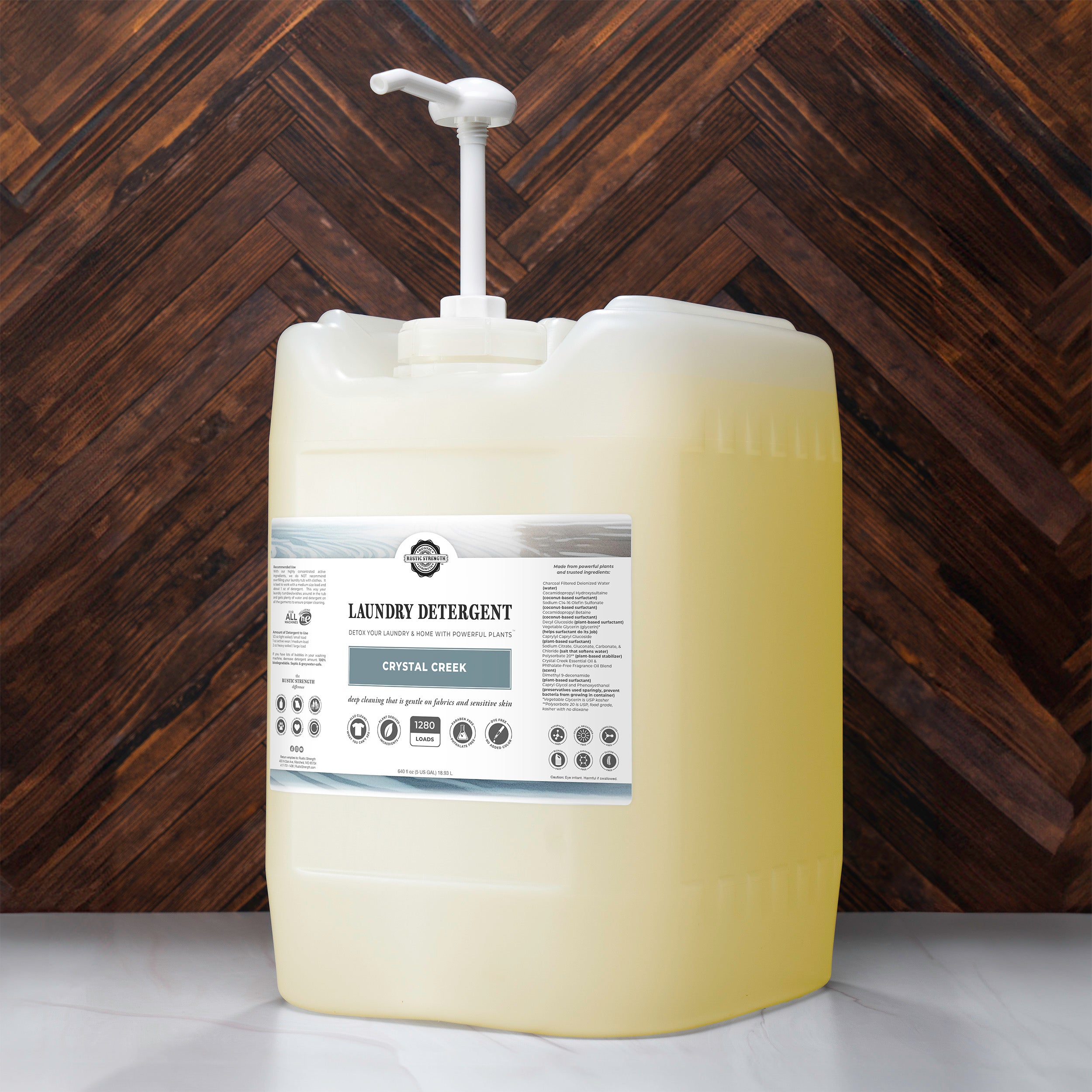 5 gallon container of Crystal Creek scented laundry detergent with pump with brown wooden background