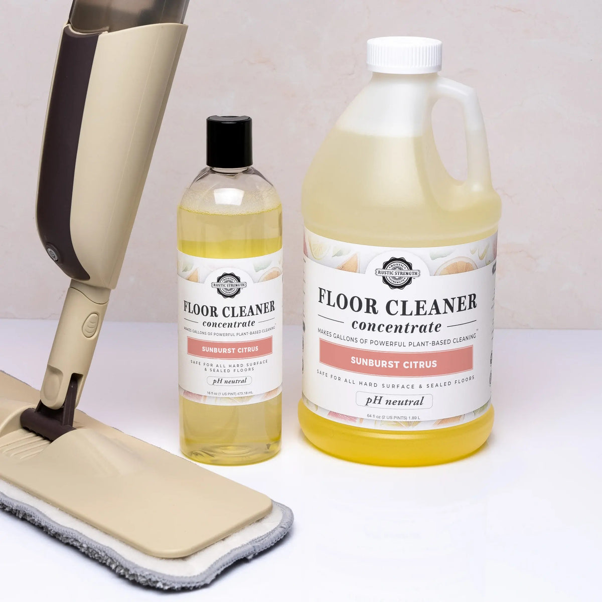 Rustic Strength, Floor Cleaner Concentrate lifestyle image picturing a Plastic Gallon and a 16oz bottle of Floor Cleaner next to a Zero Waste Mop on a marbled background.