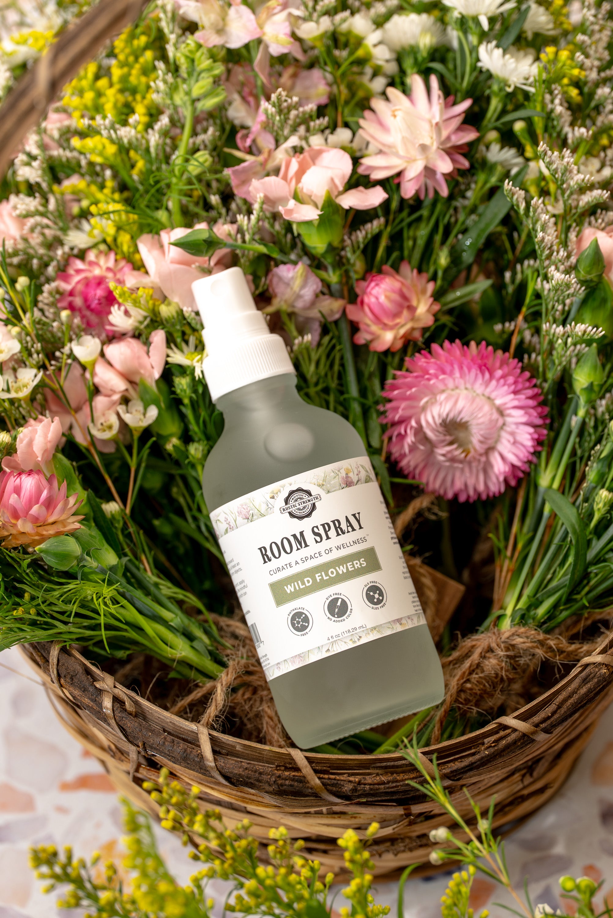 4 ounce plastic bottle of room spray in Wild Flowers scent sitting in a basket of flowers