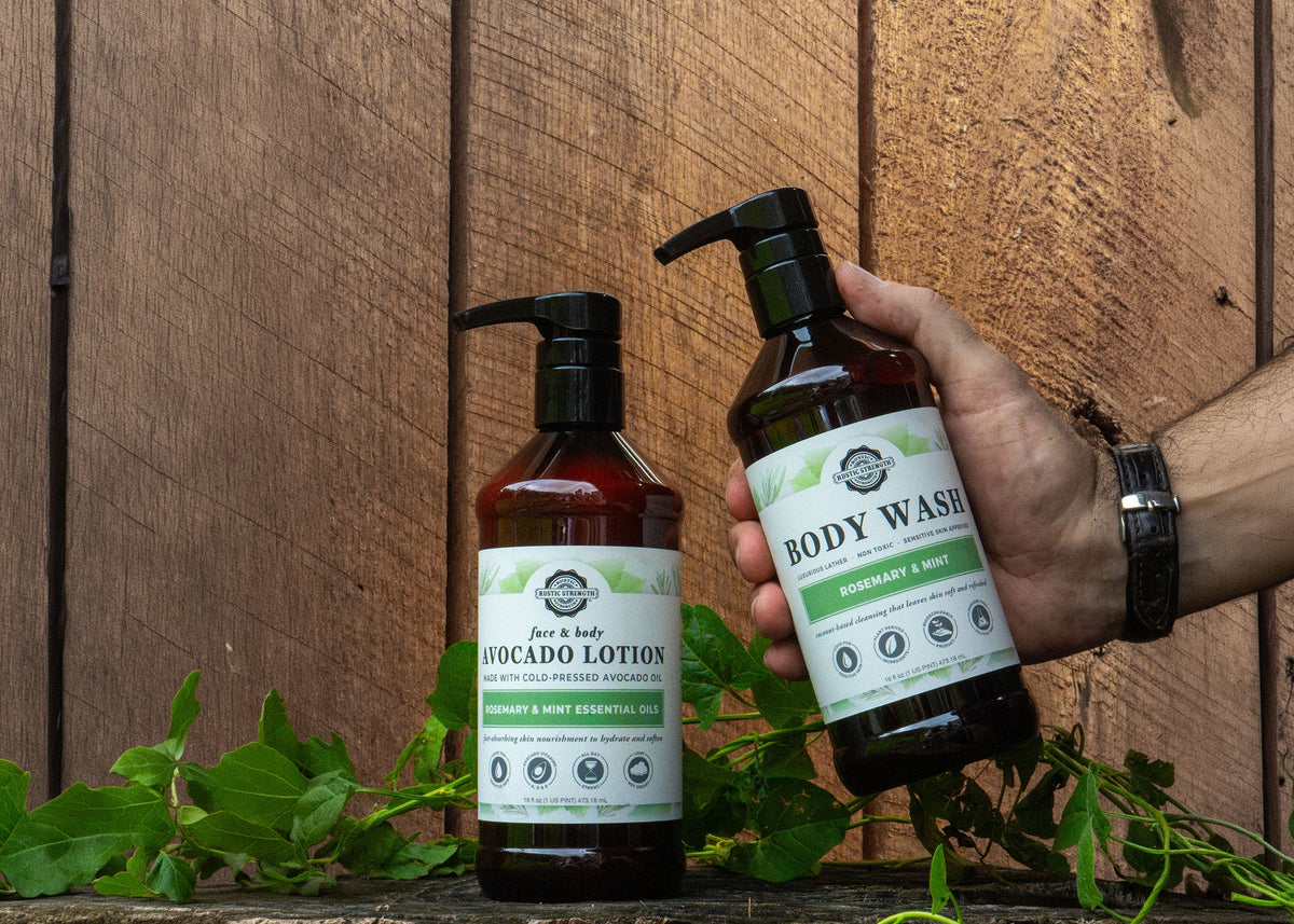 Rustic Strength, Avocado Lotion and Body Wash, 16oz Amber Bottle with black pump cap. One bottle is being held while the other sets on a lichen covered stump, in front of a wooden backdrop