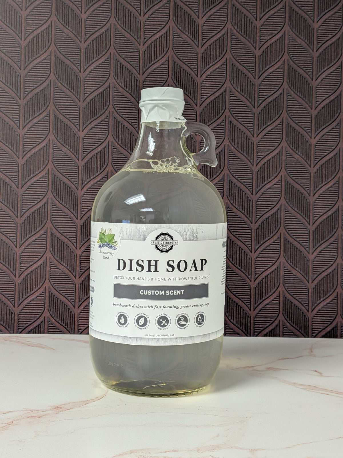 Rustic Strength, Dish Soap, Half Gallon, Glass Jug, Aromatherapy Blend, set on a light marbled surface with a patterned backdrop