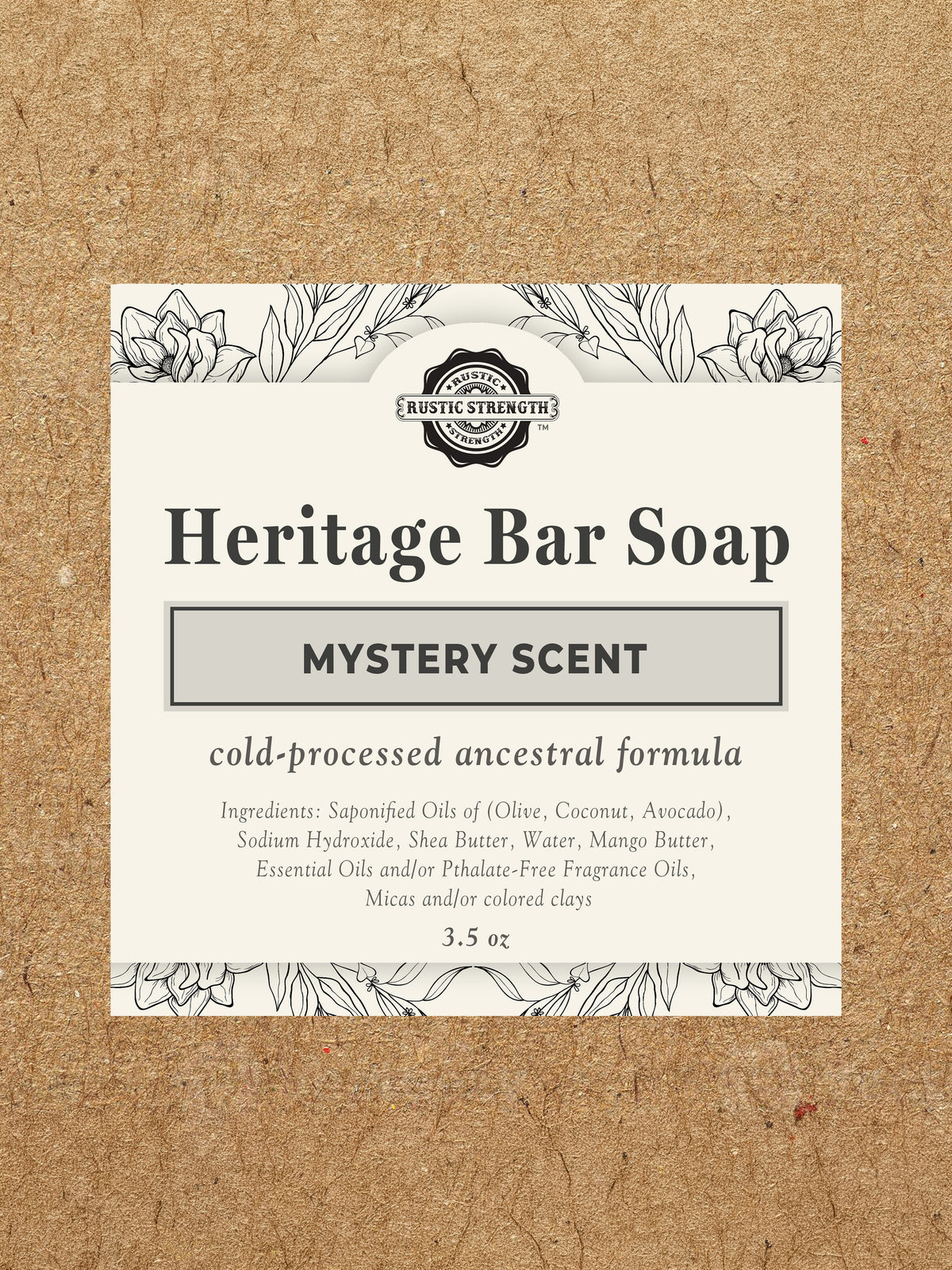 A square package of Rustic Strengths Heritage Bar Soap in Mystery Scent, featuring a cream-colored label with black text and botanical illustrations, set against a textured brown kraft paper background.